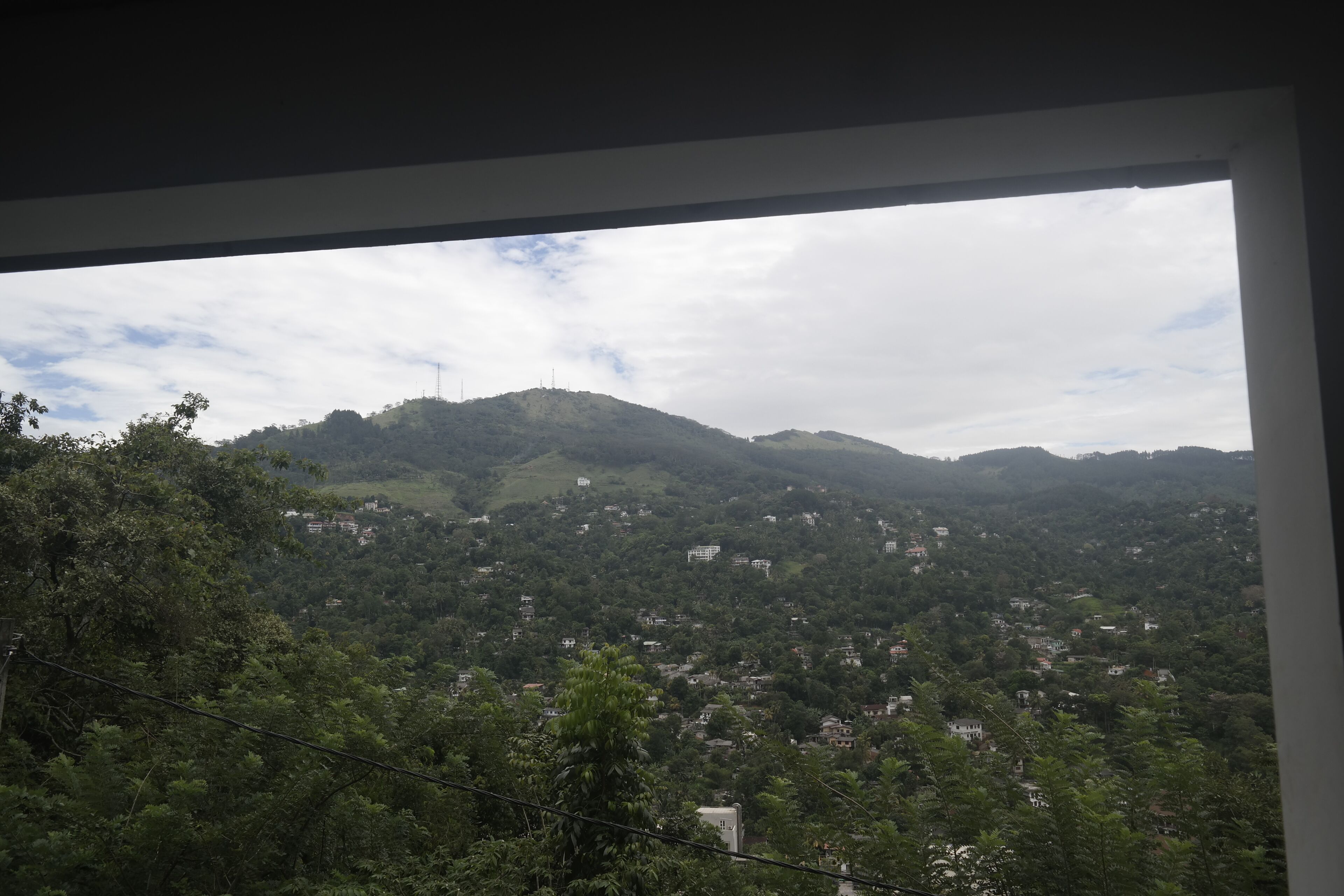 A view through a window of a mountainous landscape with scattered buildings, a clear sky, and a power line in the foreground.