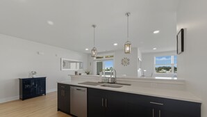 A modern kitchen with a large island, dark cabinets, and pendant lighting.