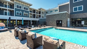 A modern building with a swimming pool, outdoor seating, and a covered area with umbrellas.