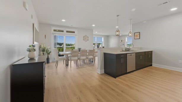 A modern kitchen with a central island, wooden flooring, and pendant lighting.