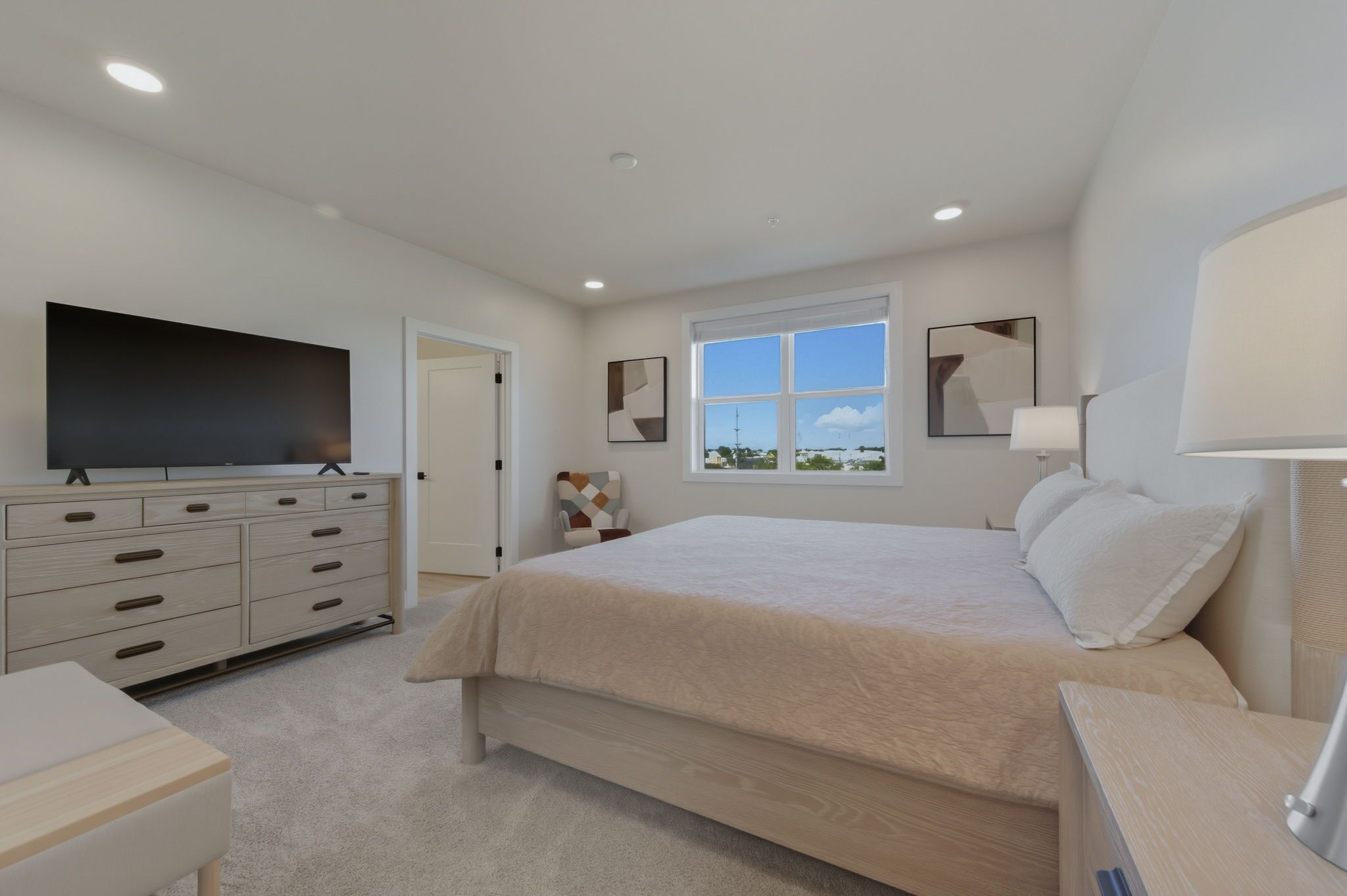 A bedroom with a large bed, a TV on a dresser, a window with a view, and a door.