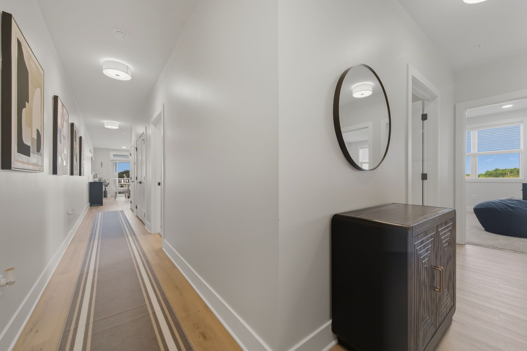A hallway with a striped carpet, a dark cabinet, and a round mirror on the wall.