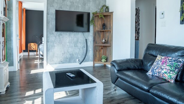 A modern living room with a black leather sofa, a white coffee table, and a TV mounted on the wall.