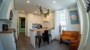 A compact kitchen with a central island, a dining area with a bench, and a view of a green door.