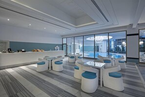 A modern hotel lobby with a reception desk, seating area with tables and chairs, and a large window overlooking a pool. - Selectum Luxury Resort Belek (Serik)