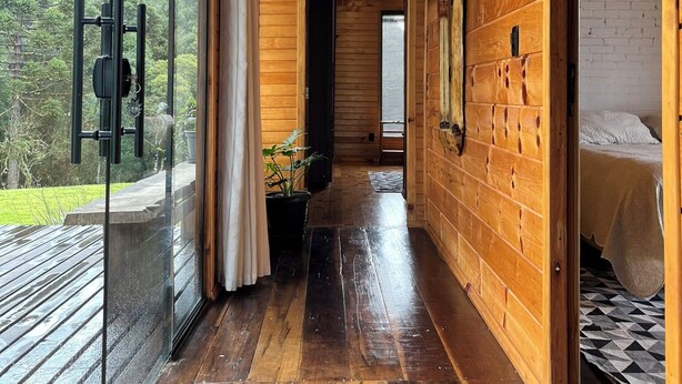 A wooden interior with a glass door leading to a balcony, a hallway, and a bed with a patterned bedspread. - Hill House - Campo Novo (Bom Retiro)