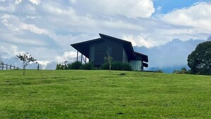 A modern building with a sloped roof, situated on a grassy field with a clear sky and scattered clouds. - Hill House - Campo Novo (Bom Retiro)