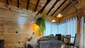 A modern living room with a wooden ceiling, a grey sofa, a dining table with chairs, and a large plant. - Hill House - Campo Novo (Bom Retiro)