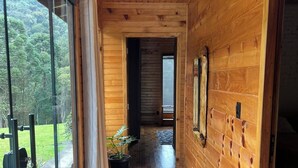 A wooden hallway with a glass door leading outside, a potted plant, and a view of greenery. - Hill House - Campo Novo (Bom Retiro)