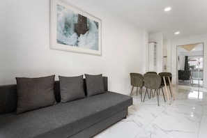 A modern living room with a grey sofa, a framed abstract painting, and a dining area with chairs and a table. - Vacation Home 'Precioso Apartamento Santa Cruz' with Wi-Fi (Santa Cruz de Tenerife)