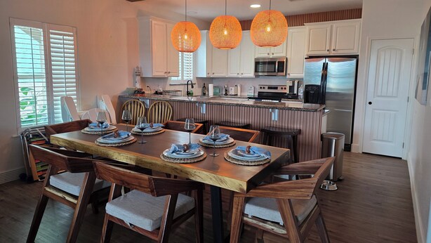 Een moderne keuken met witte kasten, een centraal eiland en een eethoek met houten stoelen en een tafel voor vier personen.