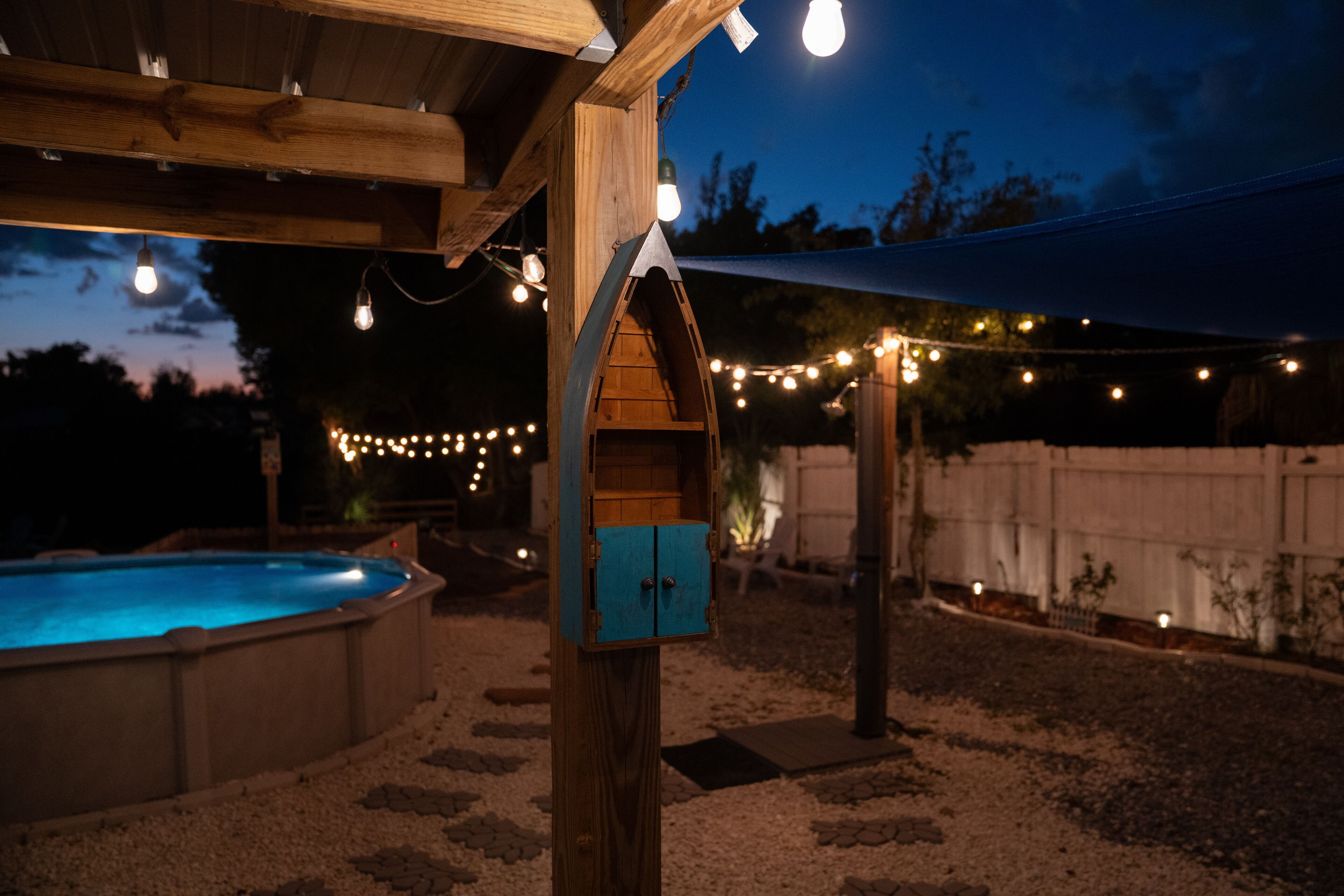 A wooden deck with a pool, string lights, and a blue birdhouse.