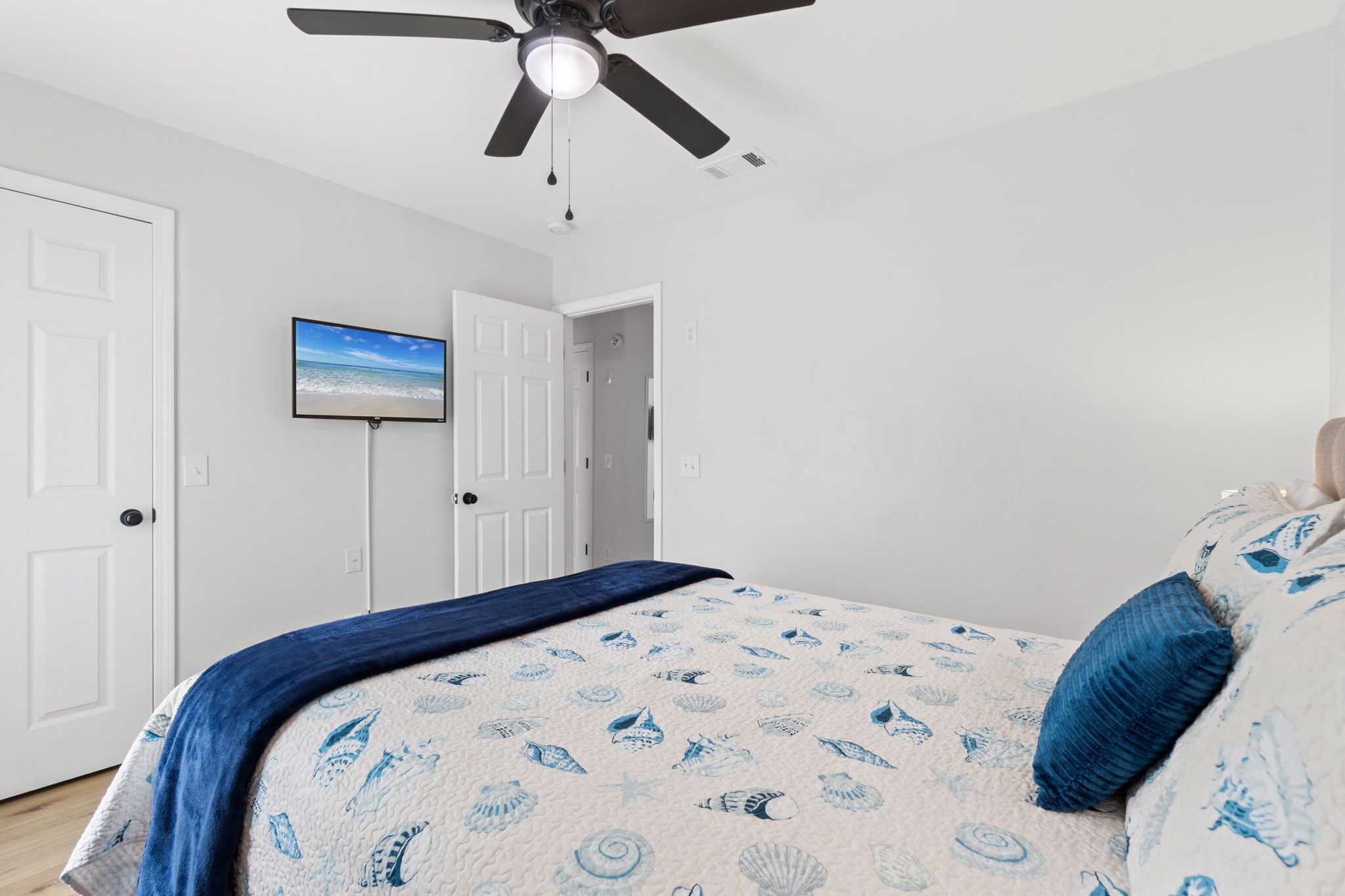 Une chambre à coucher avec un lit, un ventilateur de plafond et un téléviseur fixé au mur.