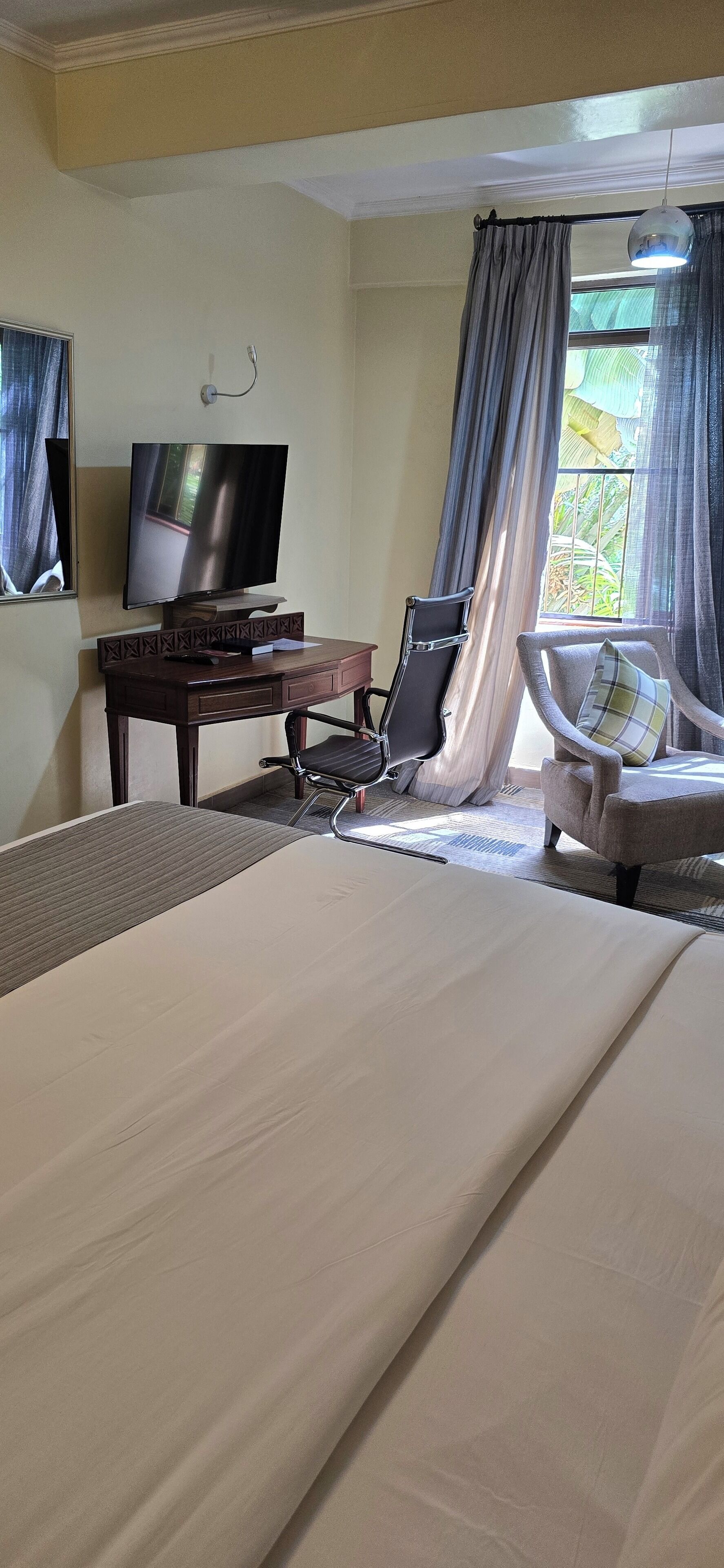 A hotel room with a bed, a desk with a television, a chair, and a window with curtains.
