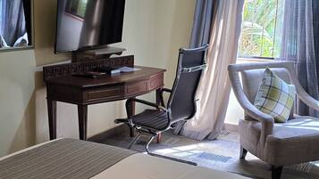 A hotel room with a bed, a desk with a television, a chair, and a window with curtains.