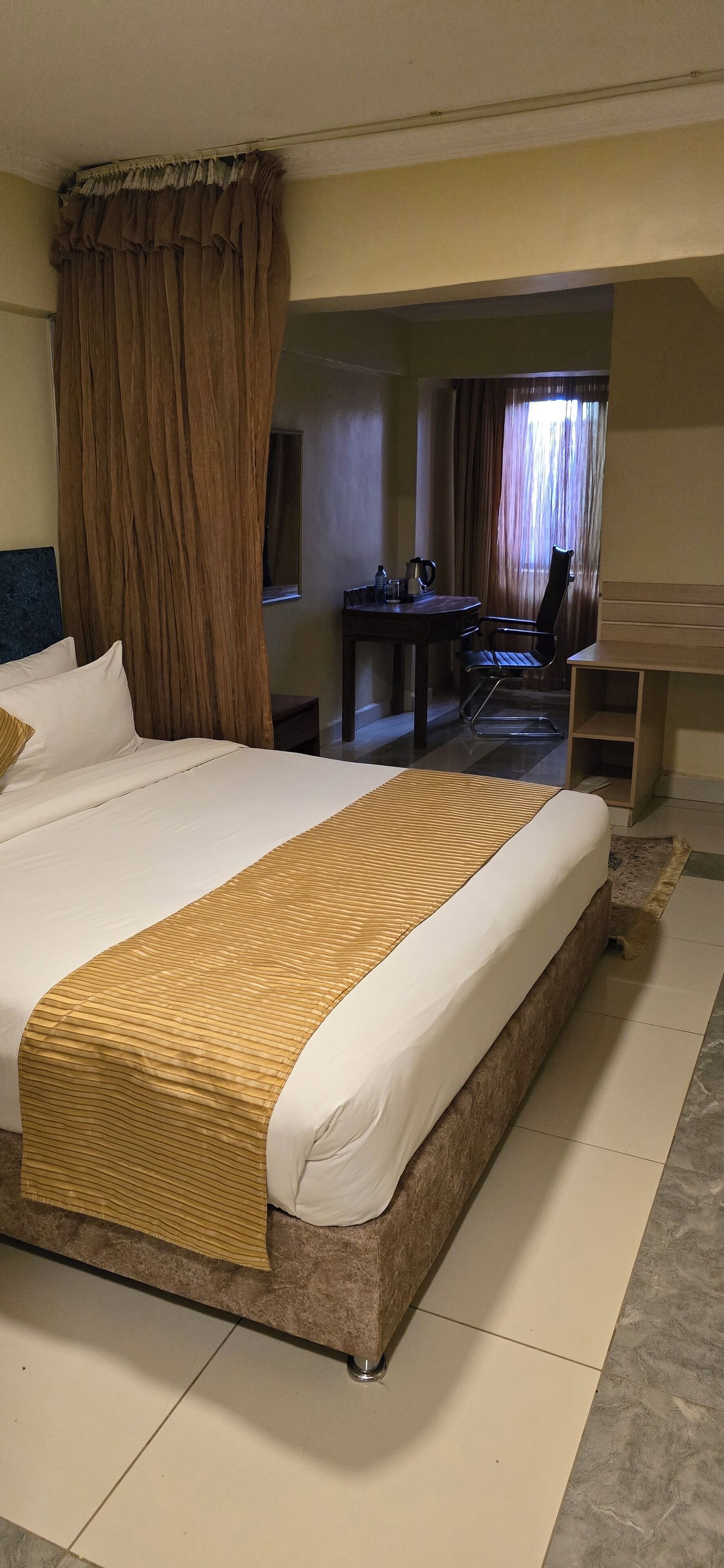 A hotel room with a large bed, a wooden headboard, a small desk, and a chair.