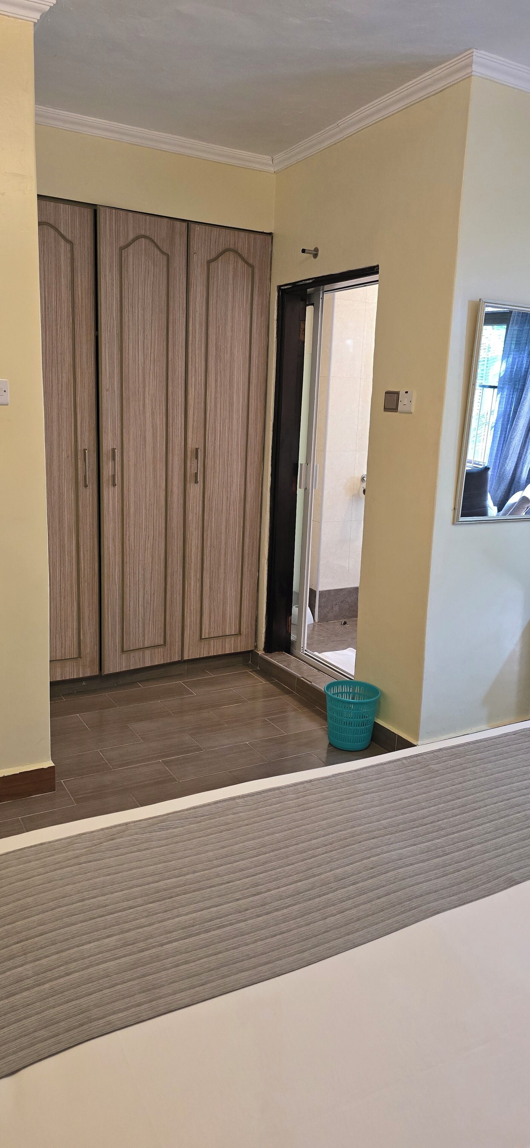 Ein Zimmer mit Holzschrank, Schiebetür, blauem Wäschekorb und einem Fenster mit Vorhängen.