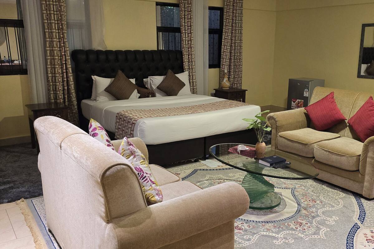 A hotel room with a bed, two sofas, a glass coffee table, and a patterned rug.