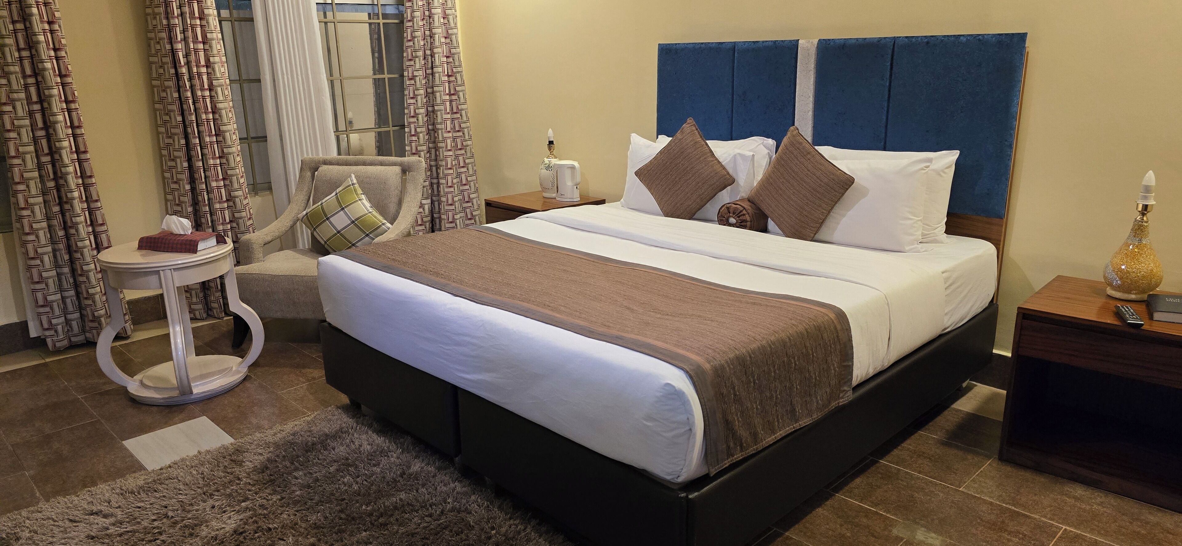 Een hotelkamer met een groot bed, een stoel, een kleine tafel en een nachtkastje met een fles en een afstandsbediening.