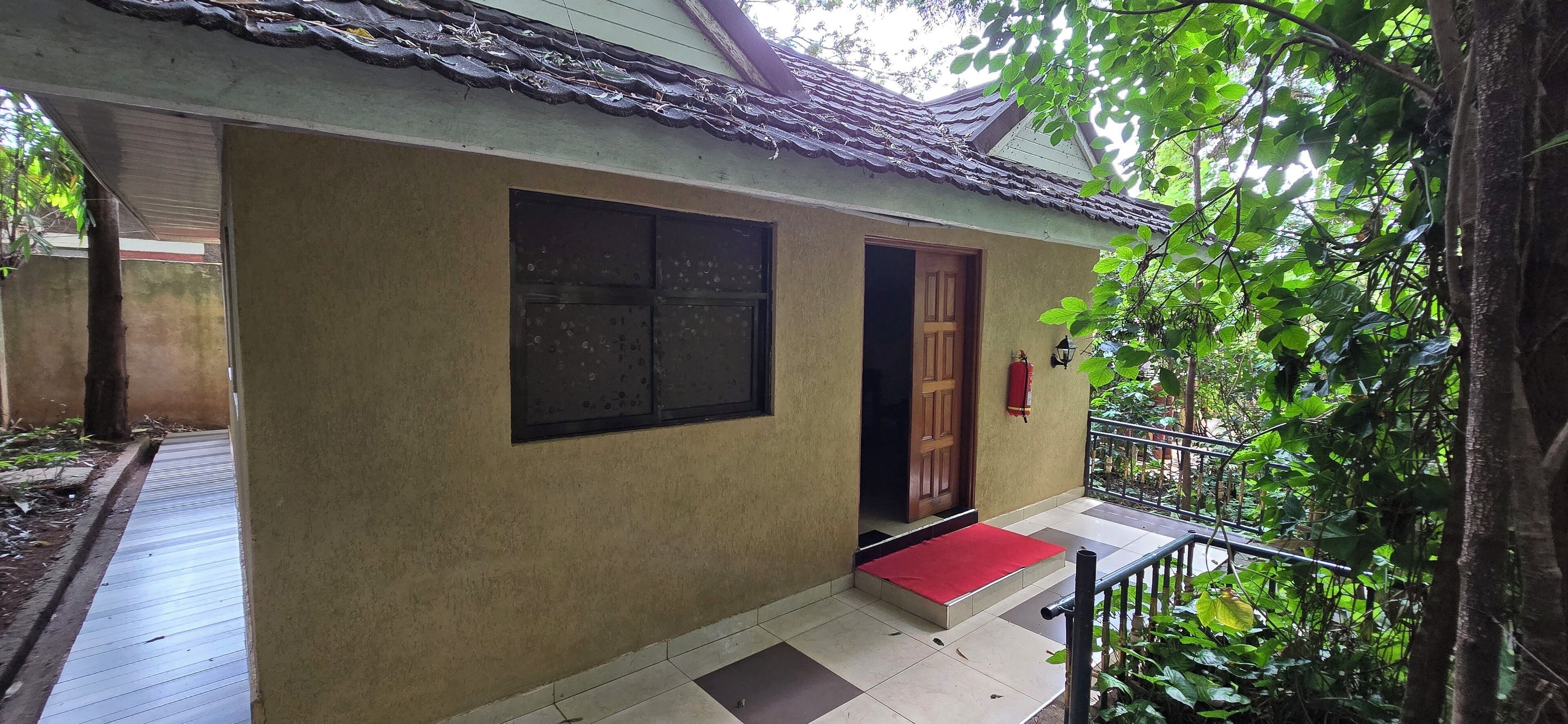 Un edificio con porche de baldosas, un felpudo rojo en la entrada y una puerta de madera.
