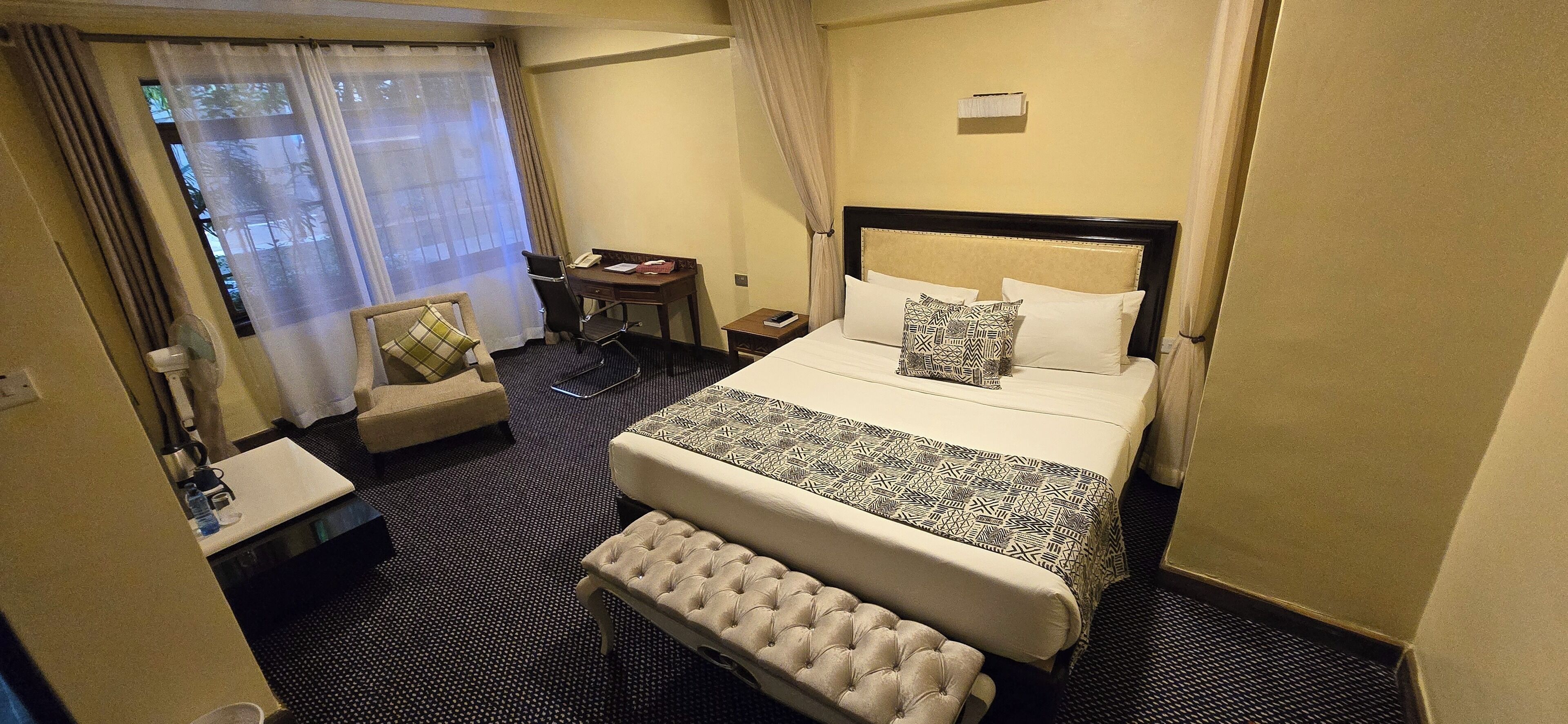 A hotel room with a bed, a desk, a chair, a small table, and a bench.