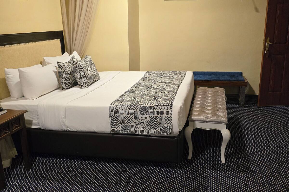 A neatly made bed with patterned bedding, a bedside table with a book, and a bench.