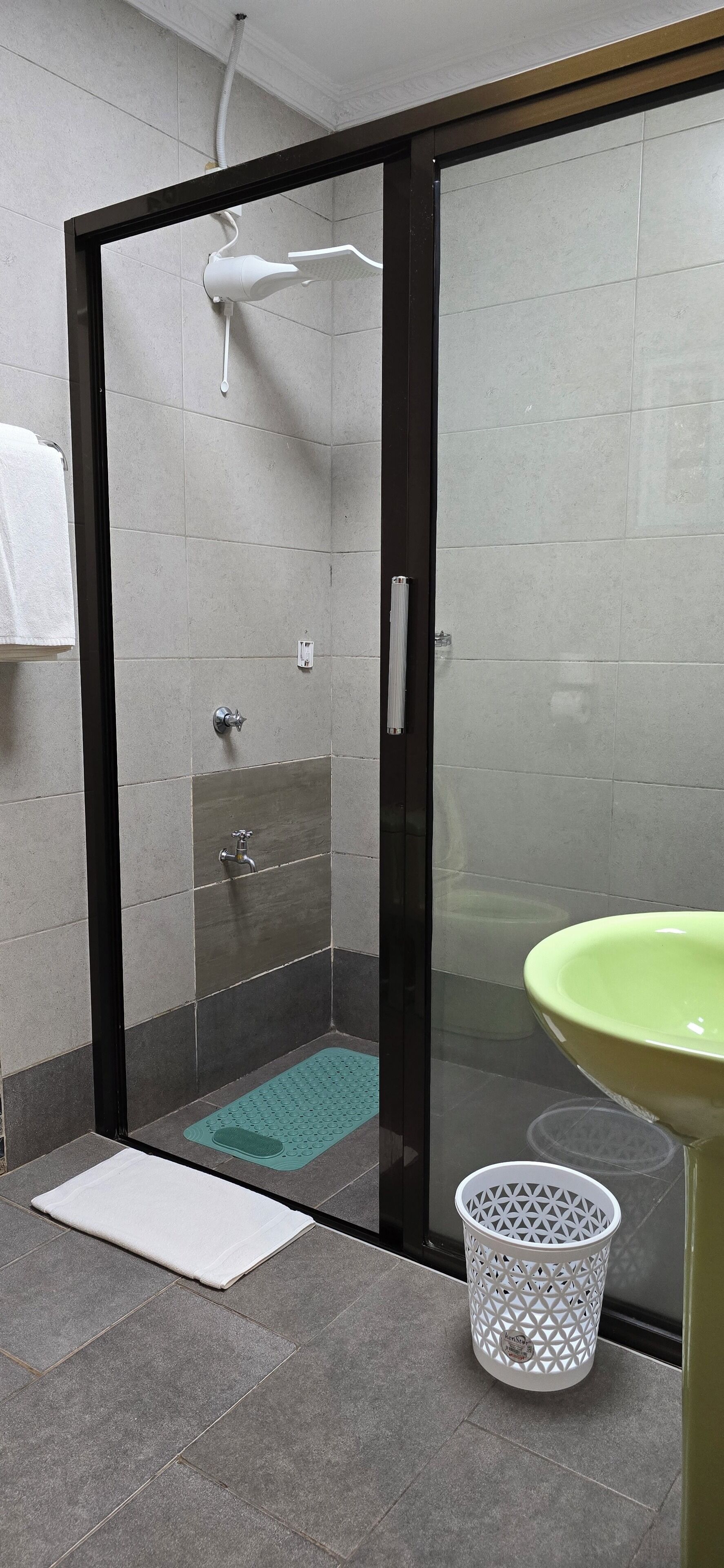 A bathroom with a glass-enclosed shower, a green sink, and a white towel rack.