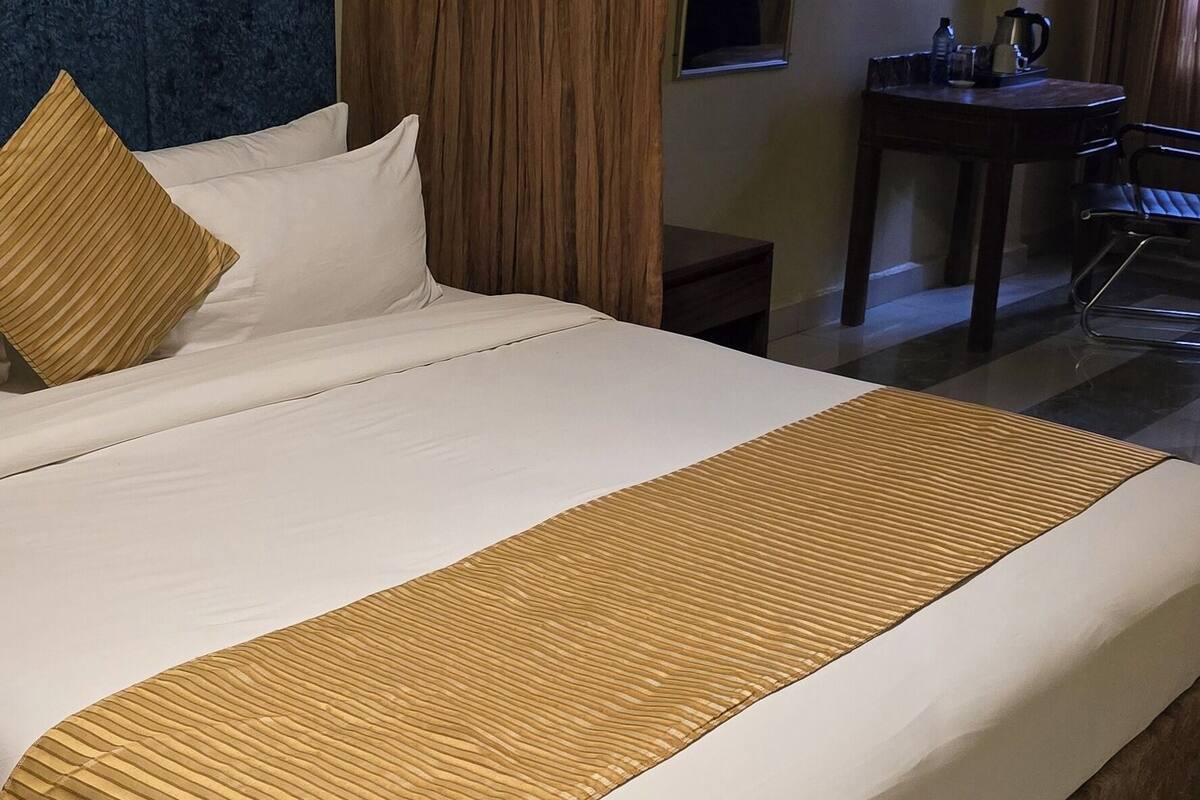 A large bed with a headboard, a bedside table with a lamp, and a window with curtains.