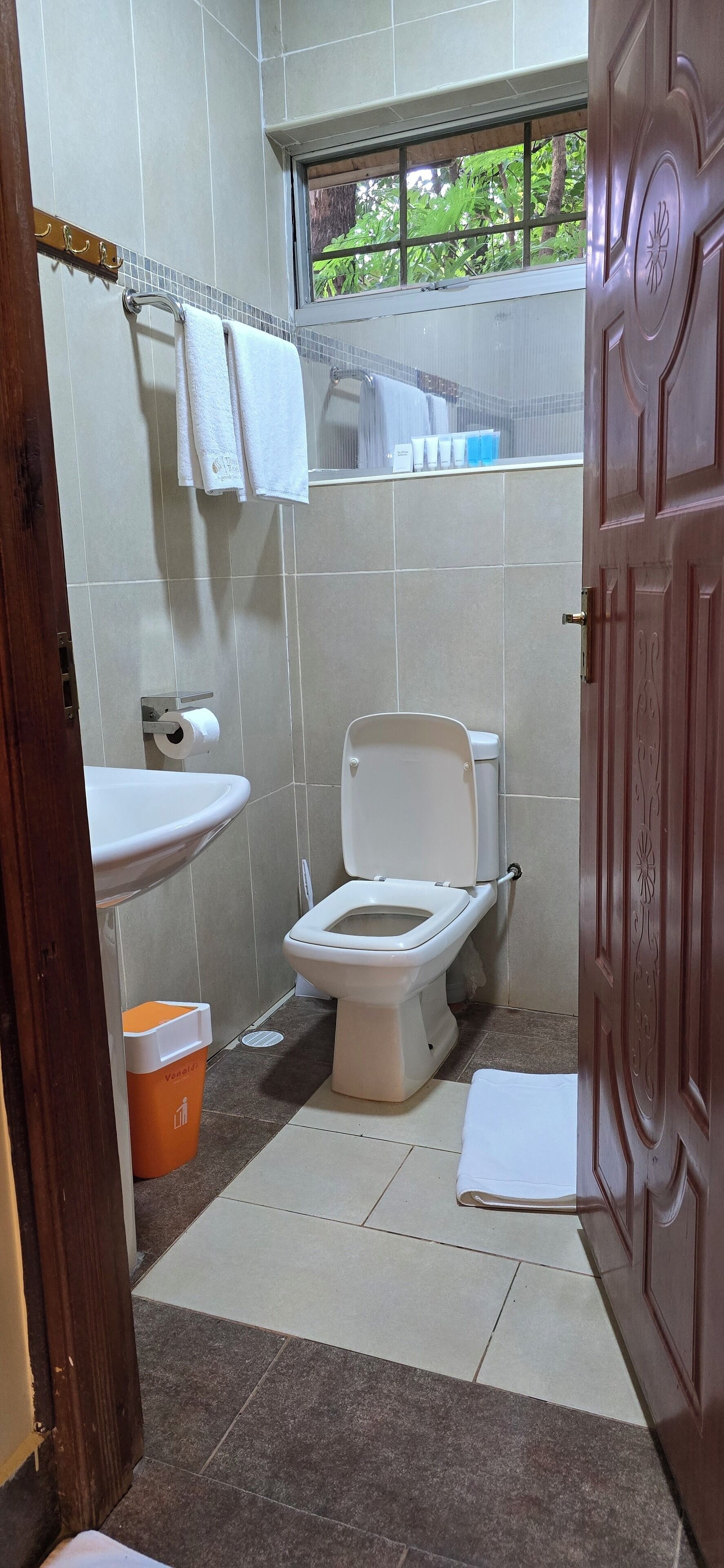 A small bathroom with a toilet, sink, and a window with a view of greenery.