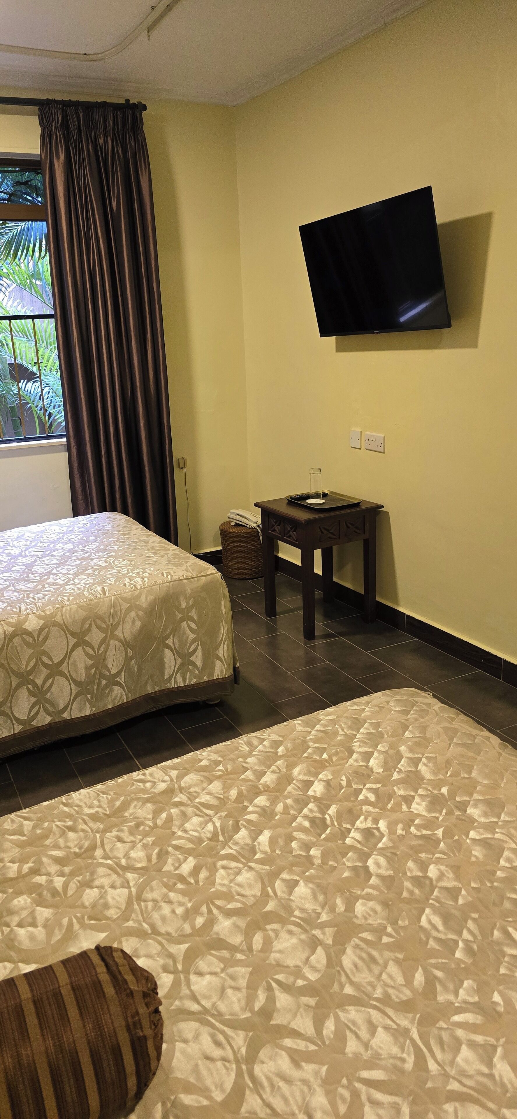 A hotel room with two beds, a TV mounted on the wall, and a small table with a basket.
