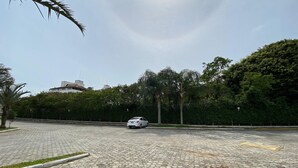 A parking area with a white car, paved with hexagonal tiles, surrounded by greenery and trees. - Apts in Condominium 40 Meters From Bombinhas Beach - Bdss (Bombinhas)