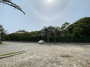 A parking area with a white car, paved with hexagonal tiles, surrounded by greenery and trees. - Apts in Condominium 40 Meters From Bombinhas Beach - Bdss (Bombinhas)