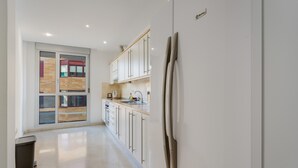 Una cocina moderna con armarios blancos, un refrigerador de acero inoxidable y una ventana con marcos de madera.
