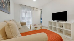 Una sala de estar moderna con un sofá, una mesa de centro, un televisor sobre un mueble bajo y una ventana con cortinas.