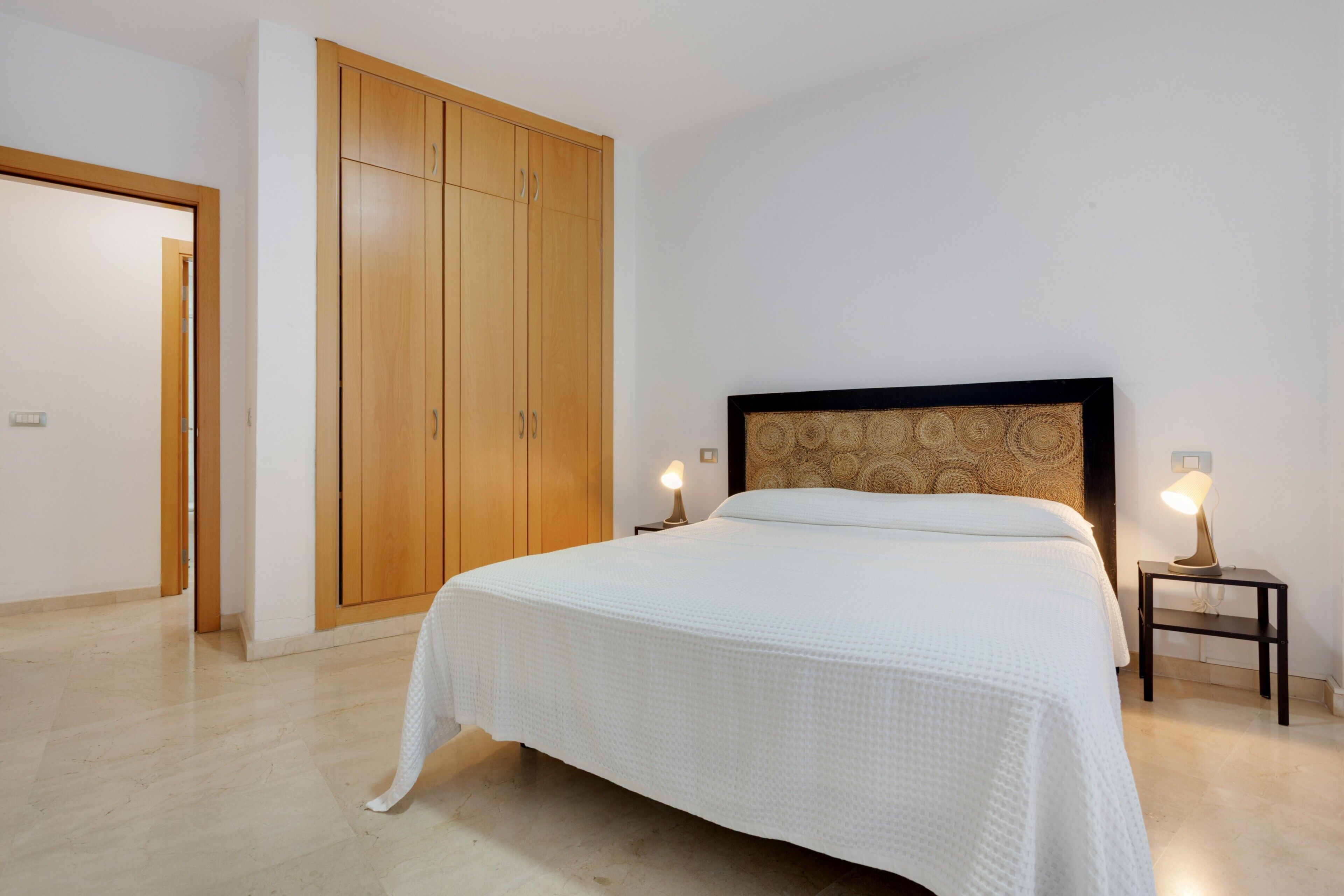 Ein Schlafzimmer mit Bett, Holzschrank, Nachttischlampen und einer Tür.