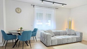 A modern living room with a grey sofa, two blue chairs, a round dining table, and a clock on the wall. - Modern apartment in the heart of Ramstein (Ramstein-Miesenbach)