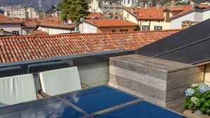 Una terraza en la azotea con una mesa de vidrio azul, asientos acolchados blancos y un banco de madera.