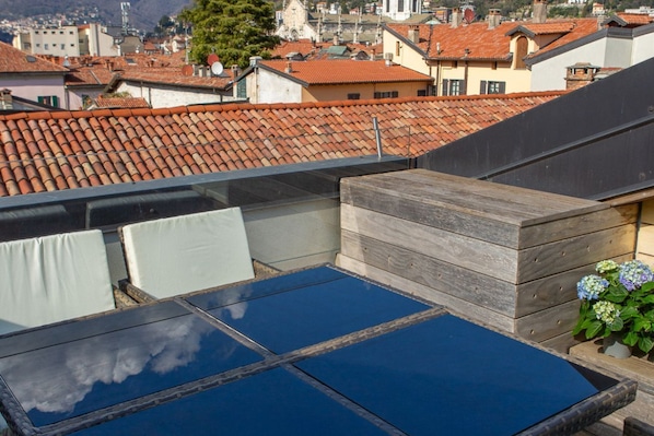 A rooftop terrace with a blue glass table, white cushioned seating, and a wooden bench. - On My Way Loft-Central Rooftop Apt with AC/Terrace (Como)