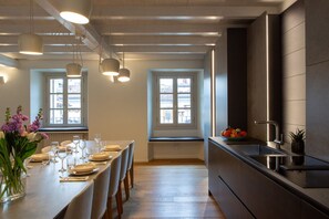 A modern kitchen with a long dining table set for six, two windows with blinds, and a built-in stove.