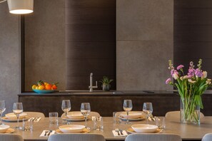 A dining area with a long table set for a meal, a bowl of fruit, a vase of flowers, and a modern light fixture.