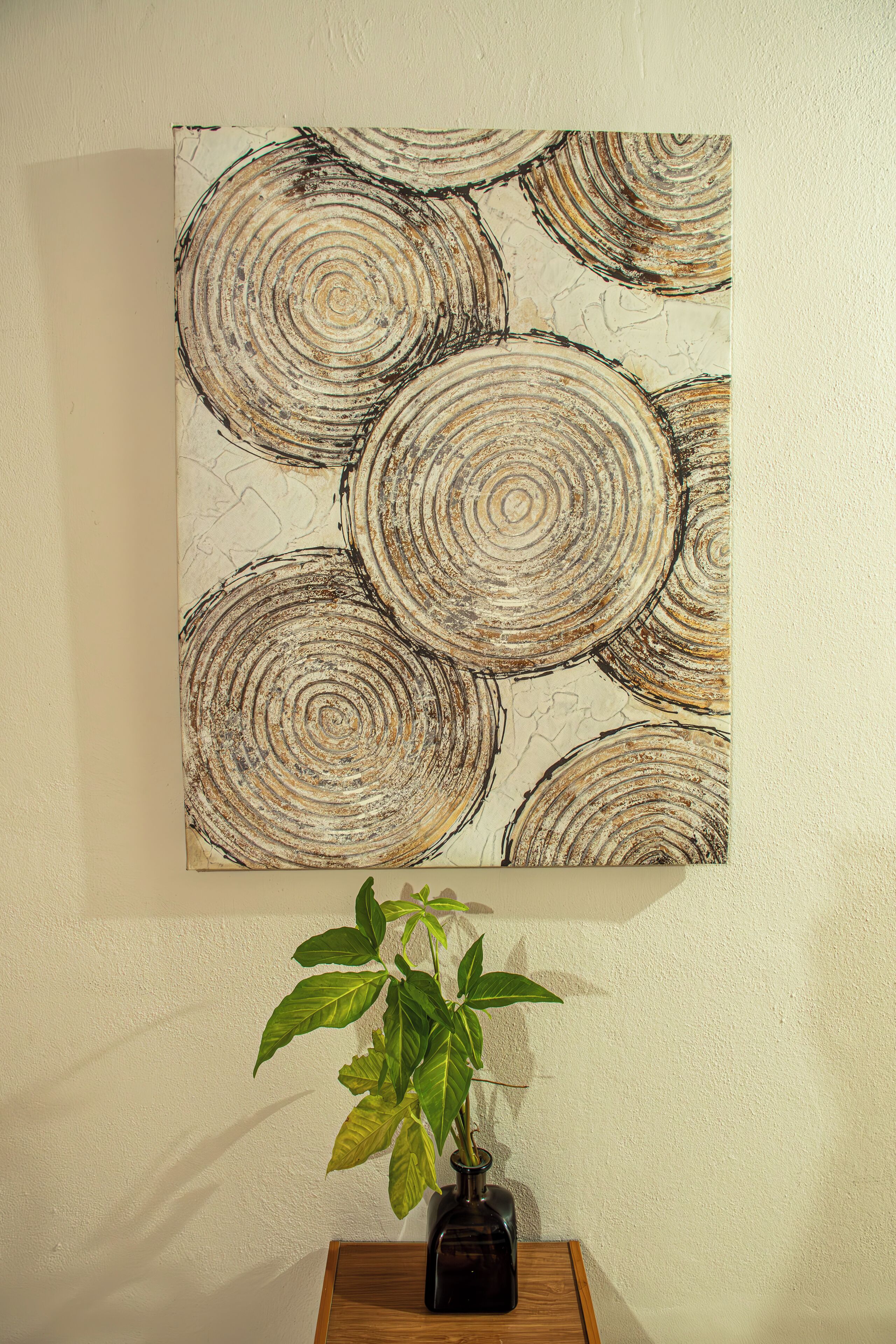 A painting of concentric circles on a wall, a potted plant, and a wooden table.