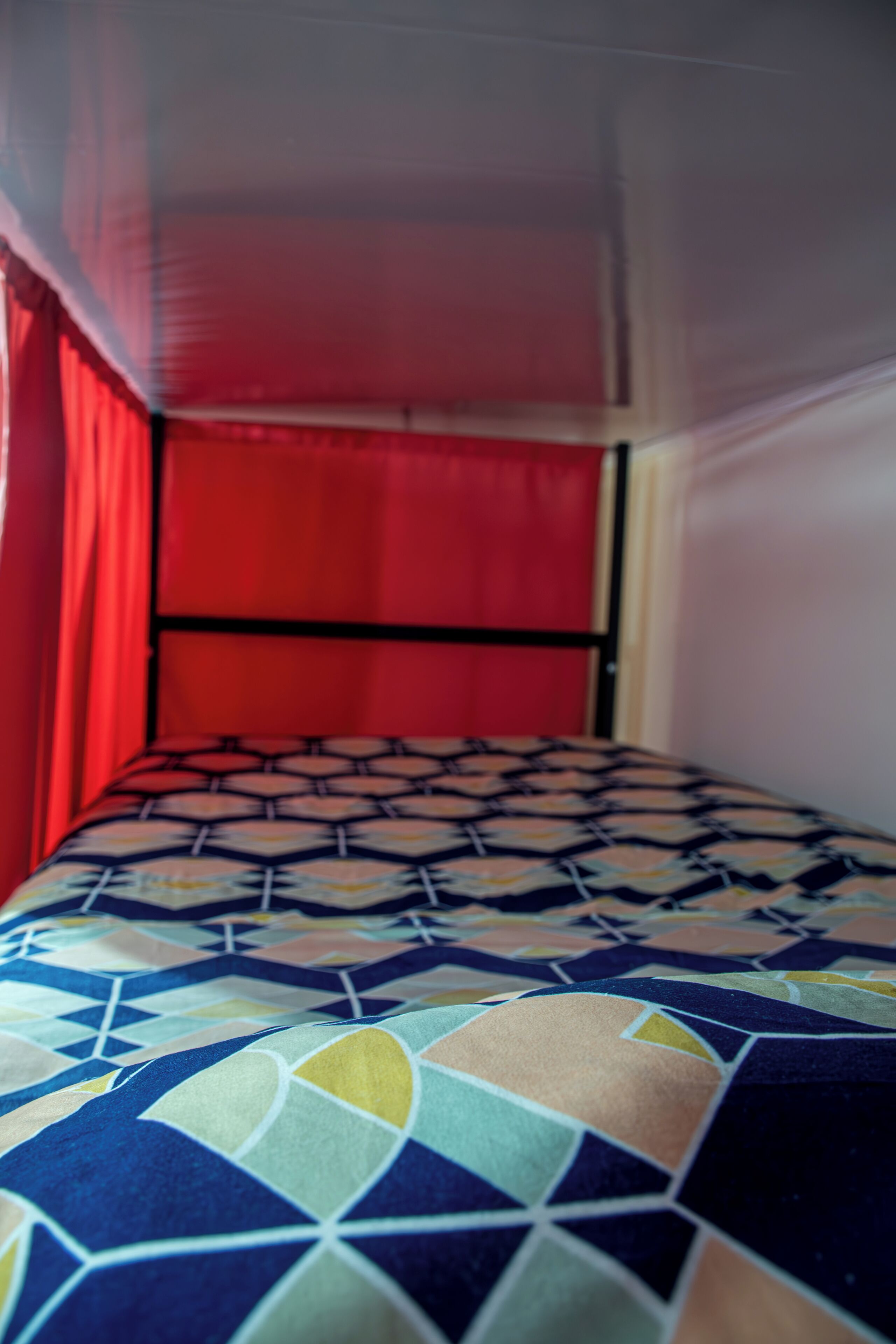 A bed with a geometric patterned bedspread, a red curtain, and a white canopy.