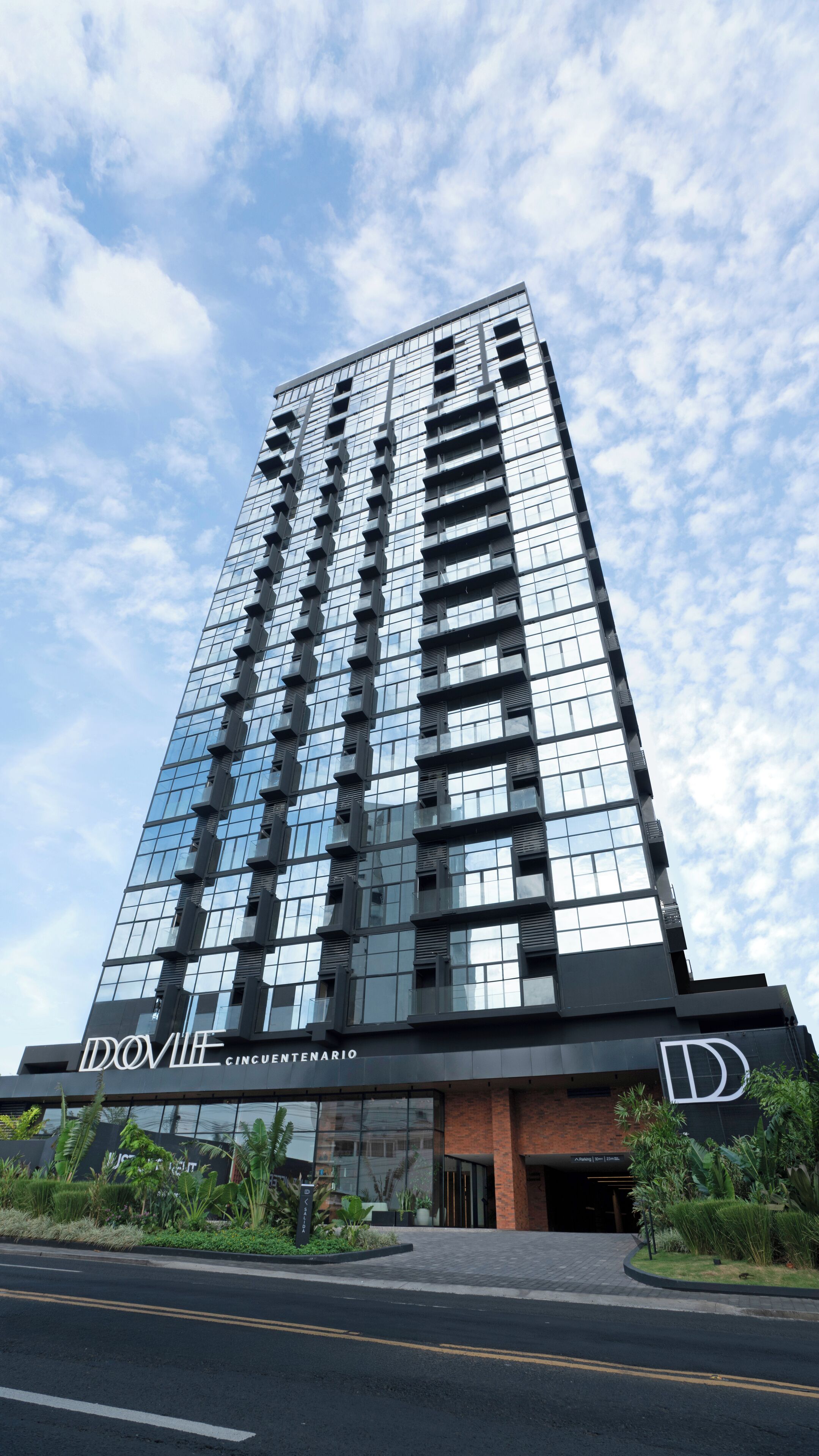 En højhusbygning med en moderne glasfacade, et markant 'D' logo, og navnet 'DOVILÉ CINCUENTENARIO' ved indgangen.