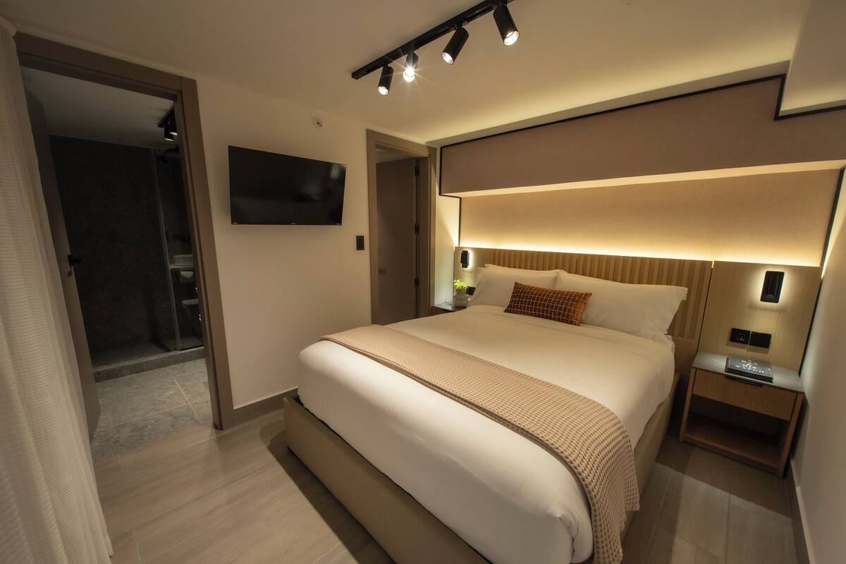 Une chambre d’hôtel moderne dotée d’un grand lit, d’un téléviseur à écran plat fixé au mur et d’une table de chevet avec une lampe.
