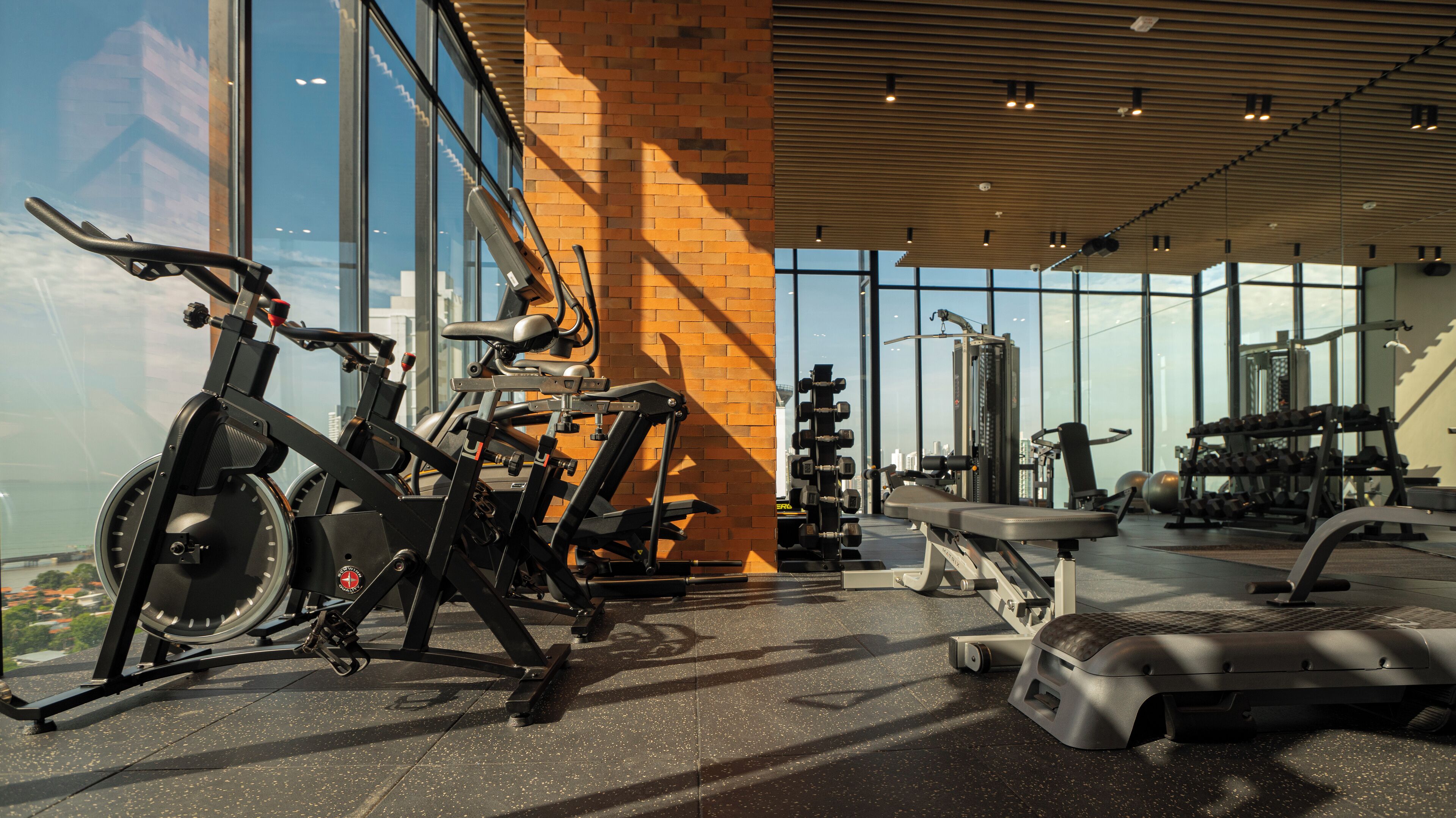 Et fitnesscenter med løbebånd, træningsmaskiner og udsigt over byen.