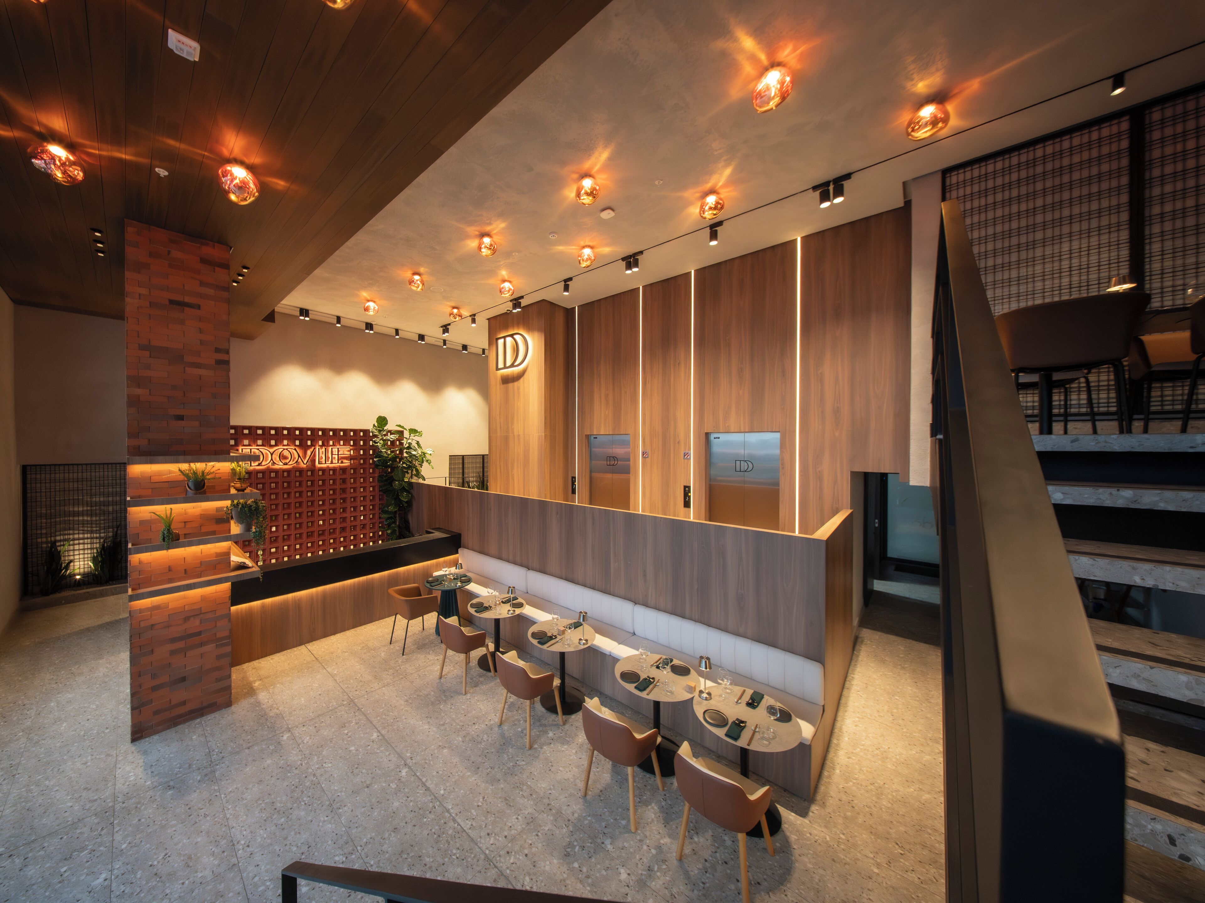Un restaurante moderno con interior de madera, una pared de acento de ladrillo y un área de comedor con mesas y sillas.
