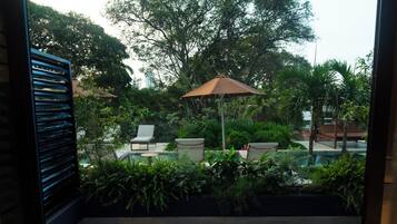 Un interior moderno con un banco de madera, dos sillas y una pared de vidrio que ofrece vistas de un jardín exterior con piscina y sombrillas.