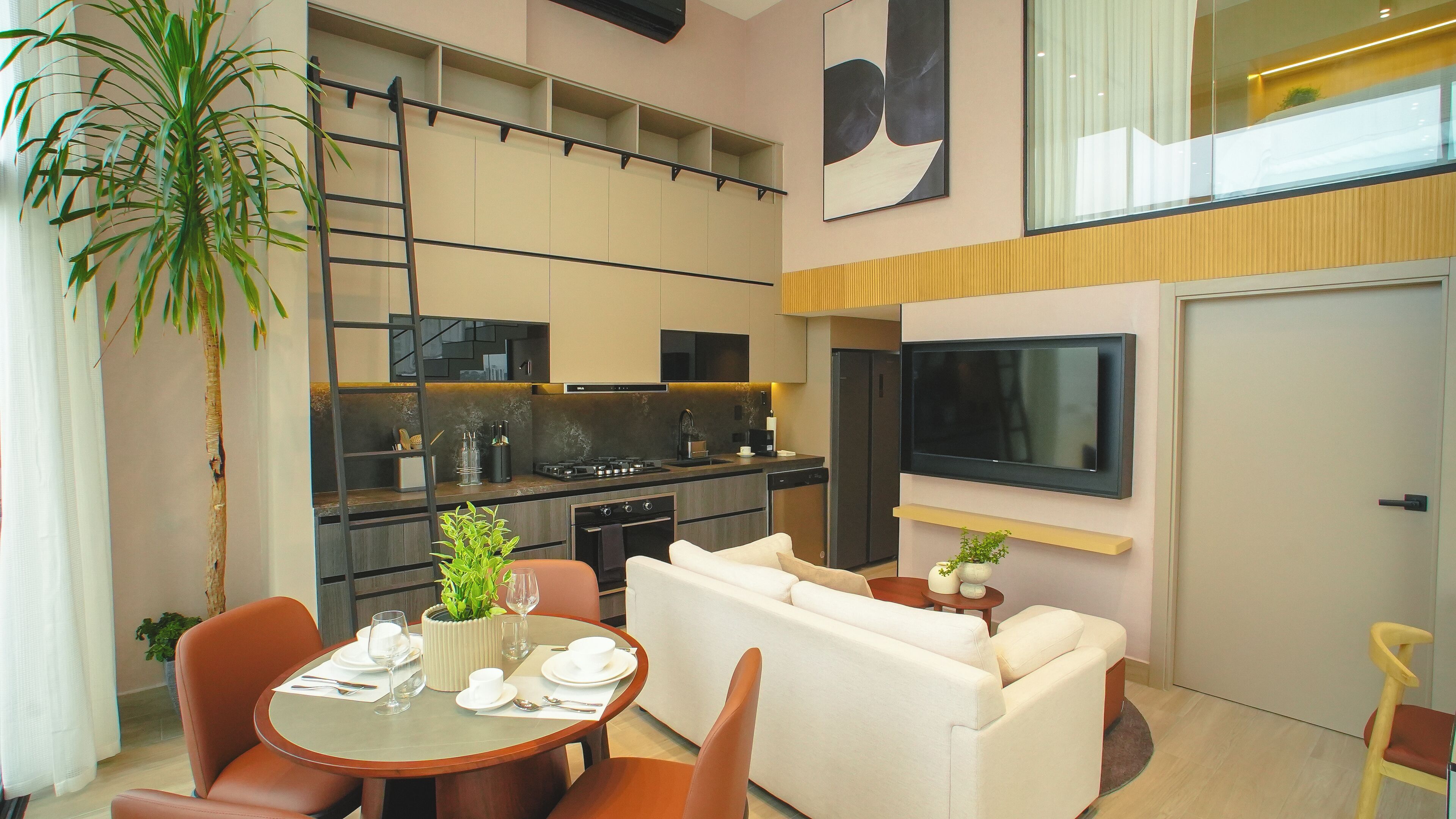 Una sala moderna con sofá, mesa de comedor para cuatro personas, zona de cocina con estufa y microondas, y un televisor de pantalla plana montado en la pared.