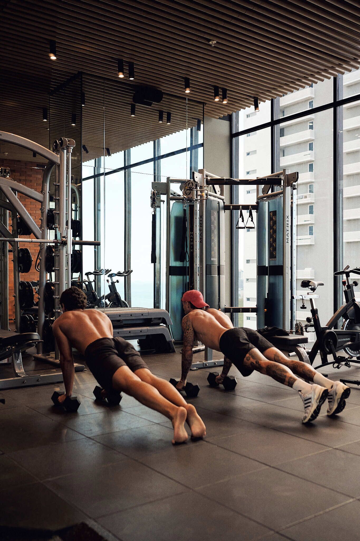 A gym with exercise equipment, large windows, and a high ceiling.