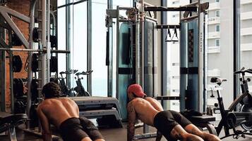 A gym with exercise equipment, large windows, and a high ceiling.